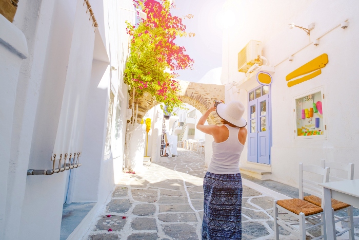 Woman in white hat walking the narrow street of the old city of Naoussa, Paros island, Greece. Girl taking photo of beautiful architecture